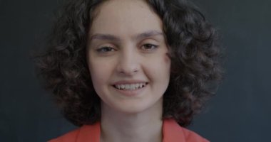 Siyah arka planda kameraya bakan gülümseyen genç bayanın portresi. Pozitif duygu ve yüz ifadesi kavramı.