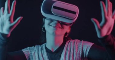Sanal gerçeklik gözlüklü kızın karanlık arka planda neon ışıkta dans etmesi. Modern alet ve eğlence konsepti.