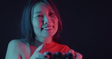 Neşeli Asyalı kadın, karanlık arka planda neon ışıkta joystick kullanarak video oyunu oynuyor. Oyun ve eğlence konsepti.