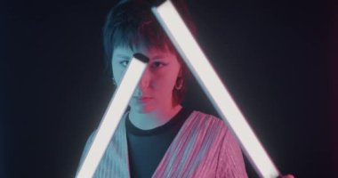 Karanlık arka planda neon lambalarla oynayan kendine güvenen Asyalı kadının yavaş çekim portresi. İnsanlar ve aydınlatma kavramı.