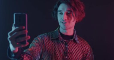 Genç adam internet üzerinden telefon görüşmesi yapıyor. Karanlık arka planda neon ışıkta sohbet ediyor. Sanal toplantı ve uzaktan iletişim konsepti.