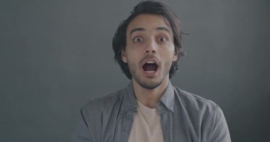 Aşırı mutlu Orta Doğulu bir adamın gri arka planda heyecanını ifade eden yavaş çekim portresi. İnsanlar ve olumlu duygu kavramı.
