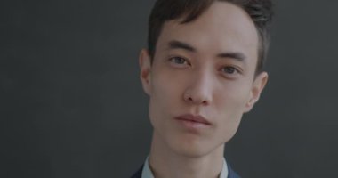 Stüdyonun arka planında duygusuz bir şekilde kameraya bakan sakin bir gencin ağır çekim portresi. İnsanlar ve yüz ifadesi kavramı.