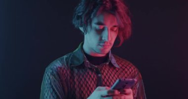 Akıllı telefon kullanan genç adam karanlık arka planda neon ışıkla sesli mesaj gönderiyor. İletişim ve modern teknoloji kavramı.
