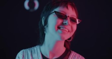Asyalı bir kızın portresi dans ediyor ve arka planda neon ışıklı sabun köpüklerini seyrediyor. Eğlence ve eğlence konsepti.