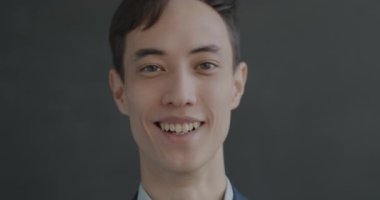 Siyah arka planda kameraya gülümseyen neşeli genç adamın yavaş çekim portresi. İyi ruh hali ve olumlu duygu kavramı.