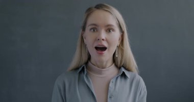 Kameraya bakan heyecanlı genç bayanın yavaş çekim portresi siyah stüdyo arka planında güzel bir sürprizin tadını çıkarıyor. İnsanlar ve olumlu duygu kavramı.