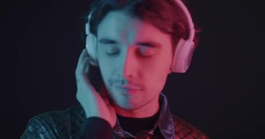 Kulaklıkla müzik dinleyen ve karanlık arka planda neon ışıkta dans eden genç adamın portresi. Gençlik kültürü ve ses aygıtı kavramı.