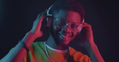 Siyah arka planda neon ışıkta dans eden kulaklıklı Afrikalı Amerikalı bir adam. Gençlik ve ses aygıtı konsepti için eğlence.
