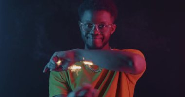 Bengal ışıklarıyla dans eden Afrikalı Amerikalı adam karanlık arka planda neon ışıkta kameraya bakıyor. Eğlence ve eğlence konsepti.