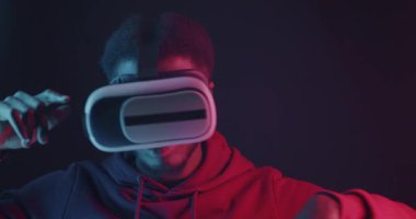 Siyah arka planda VR gözlüklü Afrikalı Amerikalı bir adam neon ışıkta dans ediyor. Sanal gerçeklik aleti ve eğlence konsepti.