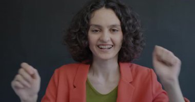 Siyah arka planda kameraya bakarak dans eden mutlu genç bir kadının yavaş çekim portresi. Parti zamanı ve eğlence konsepti.