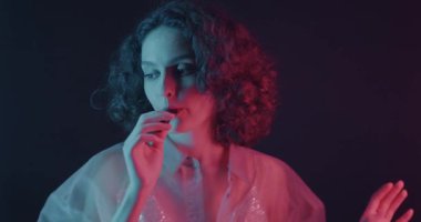 Güzel genç bir kadın karanlık arka planda neon ışıkta vapur yapıp dans ediyor. Elektronik sigara ve insanlar konsepti.