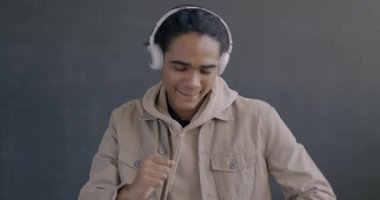 Siyah arka planda dans eden kulaklıkla müzik dinleyen mutlu Afro-Amerikan bir adamın yavaş çekim portresi. İnsanlar ve eğlence konsepti.