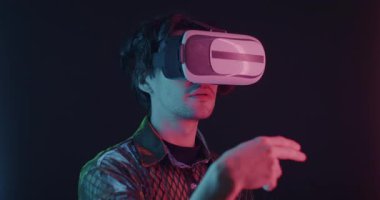 Sanal gerçeklik gözlüklü genç adam karanlık arka planda neon ışığı altında duran elleri hareket ettiriyor. Eğlence ve artırılmış gerçeklik kavramı.