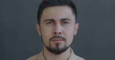 Gri arka planda gerilim hisseden endişeli, çift ırklı bir adamın yavaş çekim portresi. İnsanlar ve olumsuz duygu kavramı.