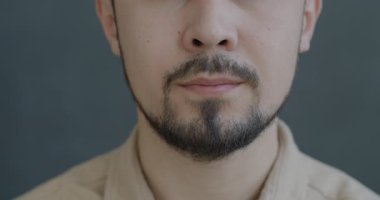 Gri arka planda gülümseyen isimsiz genç adamın yavaş çekimleri. Pozitif duygu ve insanların kavramı.