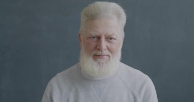 Mutsuz yaşlı bir adamın yavaş çekim portresi baş aşağı el hareketi gösteriyor siyah renkli arka planda kameraya bakarak başını sallıyor..