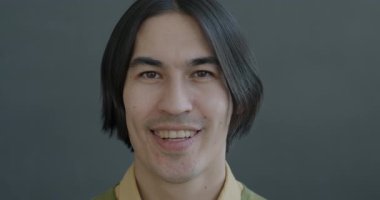 Siyah arka planda kameraya bakıp eğlenen neşeli Asyalı adamın yavaş çekim portresi. İnsanlar ve olumlu duygu kavramı.