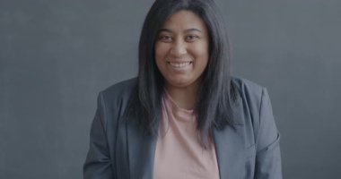 Dost canlısı genç bir kadının el sallayıp siyah arka planda kameraya bakarken gülümsemesinin yavaş çekim portresi. İnsanlar ve duygu kavramı.