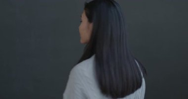 Siyah arka planda gülümseyen genç ve güzel Asyalı bir kadının yavaş çekim portresi. Pozitif duygu ve bireysel tarz kavramı.