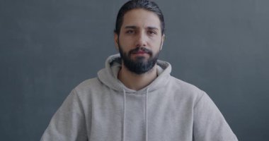 Orta Doğulu mutsuz bir adamın yavaş hareket eden portresi. Gri arka planda el hareketleriyle başını sallıyor. İnsanlar ve olumsuz duygu kavramı.