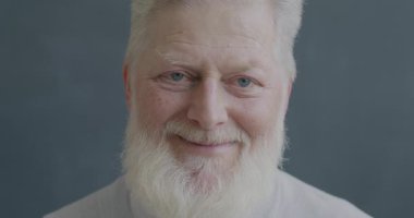 Siyah arka planda kameraya bakarak gülümseyen neşeli yaşlı adamın yavaş çekim portresi. İnsanlar ve olumlu duygu kavramı.