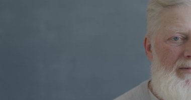 Siyah arkaplanda duygusuz bir şekilde kameraya bakan yaşlı bir adamın yavaş çekim portresi. İnsanlar ve ifade kavramı.