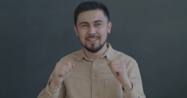 Gri arka planda eğlenen kameraya bakarak dans eden neşeli melez adamın yavaş çekim portresi. İnsanlar ve iyi ruh hali kavramı.