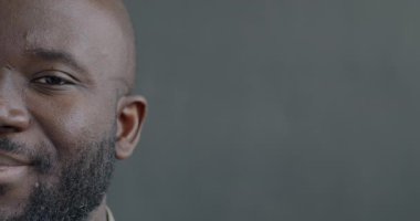 Gri arka planda kameraya bakan mutlu Afro-Amerikan bir adamın yavaş çekim portresi. Pozitif duygu ve insanların kavramı.