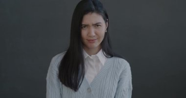 Mutsuz genç Asyalı kadının yavaş hareket eden portresi. Siyah arka planda baş sallayarak el hareketi gösteriyor.