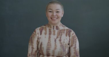 Siyah arka planda kameraya bakıp el hareketi yapan neşeli, genç Asyalı kadının yavaş çekim portresi.