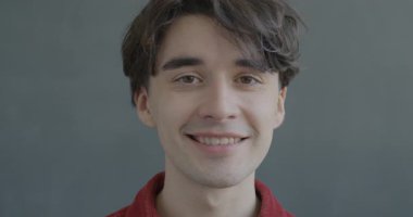 Kameraya bakıp gülümseyen, siyah renkli arka planda mutlu hisseden neşeli bir gencin yavaş çekim portresi. İnsanlar ve iyi ruh hali kavramı.