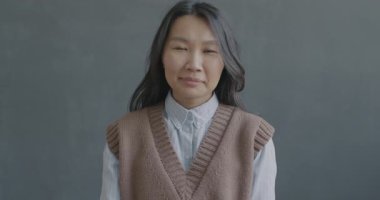 Neşeli Asyalı kadının el sallayan ve siyah arka planda kameraya bakan gülümseyen yavaş hareket portresi. İnsanlar ve duygu kavramı.