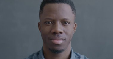 Siyah arka planda kameraya bakıp gülen neşeli Afrikalı Amerikalı adamın yavaş çekim portresi. İnsanlar ve mutluluk kavramı.