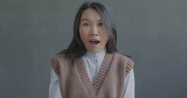 Aşırı sevinçli ve şaşırmış Asyalı kadının yavaş çekimde çekilmiş portresi siyah arka planda ağzını açan kameraya bakıyor. İnsanlar ve duygu kavramı.