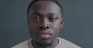 Gri arka planda kameraya bakan kasvetli Afrikalı Amerikalı adamın yavaş çekim portresi. İnsanlar ve olumsuz duygu kavramı.