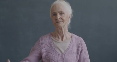 Siyah arkaplandaki kameraya bakarak el hareketi yapan hoşnutsuz yaşlı bir kadının ağır çekim portresi..