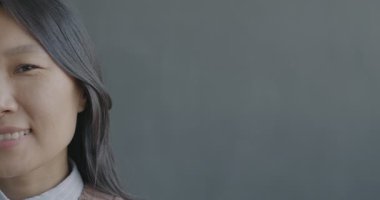 Siyah arka planda gülümseyen kameraya bakan mutlu Asyalı kadının yavaş çekim portresi. İnsanlar ve duygu kavramı.