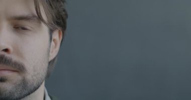 Siyah arka planda duygusuz bir şekilde kameraya bakan genç bir adamın yavaş çekim portresi. İnsanlar ve ifade kavramı.