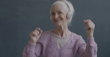 Kulaklıkla müzik dinleyen ve siyah renkli arka planda dans eden mutlu son sınıf kadınının yavaş çekim portresi. İnsanlar ve eğlence konsepti.