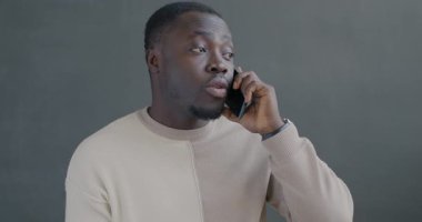 Afro-Amerikalı bir adam cep telefonuyla konuşuyor. Siyah arka planda el kol hareketi yapıyor. İletişim ve insan kavramı.