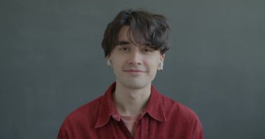 Çevrimiçi video konuşması yapan neşeli bir gencin portresi kameraya bakarak siyah arkaplanda kablosuz kulaklık kullanıyor..