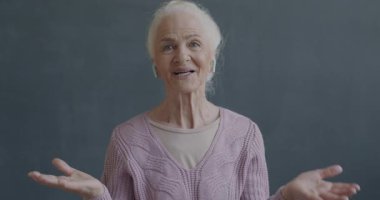 Çevrimiçi video görüşmesi yapan neşeli son sınıf kadınının portresi siyah arkaplanda kablosuz kulaklık kullanarak kameraya bakıp el kol hareketi yapıyor..