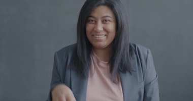 Tatmin olmuş genç bir kadının yavaşça portresi. Siyah arka planda kameraya gülümseyen el hareketi gösteriyor. İnsanlar ve olumlu duygu kavramı.