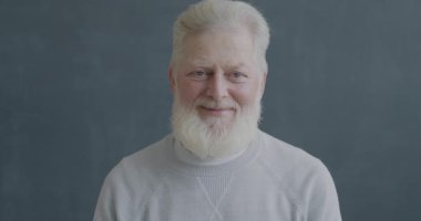 Siyah arka plandaki kameraya bakarak el sallayan ve gülümseyen son sınıf öğrencisinin yavaş çekim portresi. İnsanlar ve duygu kavramı.