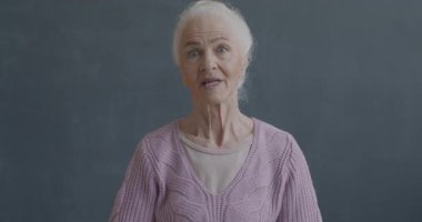 Siyah arka planda ağzı açık kameraya bakan yaşlı bir kadının yavaş çekim portresi. İnsanlar ve duygu kavramı.