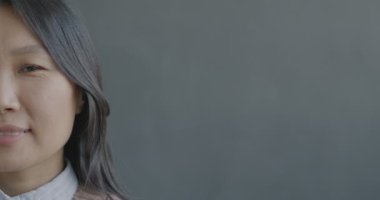 Siyah arka planda gülümseyen kameraya bakan neşeli Asyalı bayanın yavaş çekim portresi. İnsanlar ve olumlu duygu kavramı.