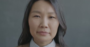 Siyah arka planda gülümseyen kameraya bakan neşeli Asyalı kadının yavaş çekim portresi. İnsanlar ve yüz ifadesi kavramı.