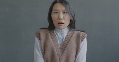 Korkmuş Asyalı kadının yavaş çekim portresi. Kameraya bakıyor ve kötü sürprizin ardından başını sallıyor. Siyah arka planda duruyor..